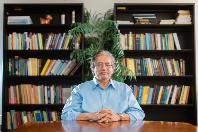 Headshot of Carlos Castillo-Chavez sitting at a desk with books behind it.