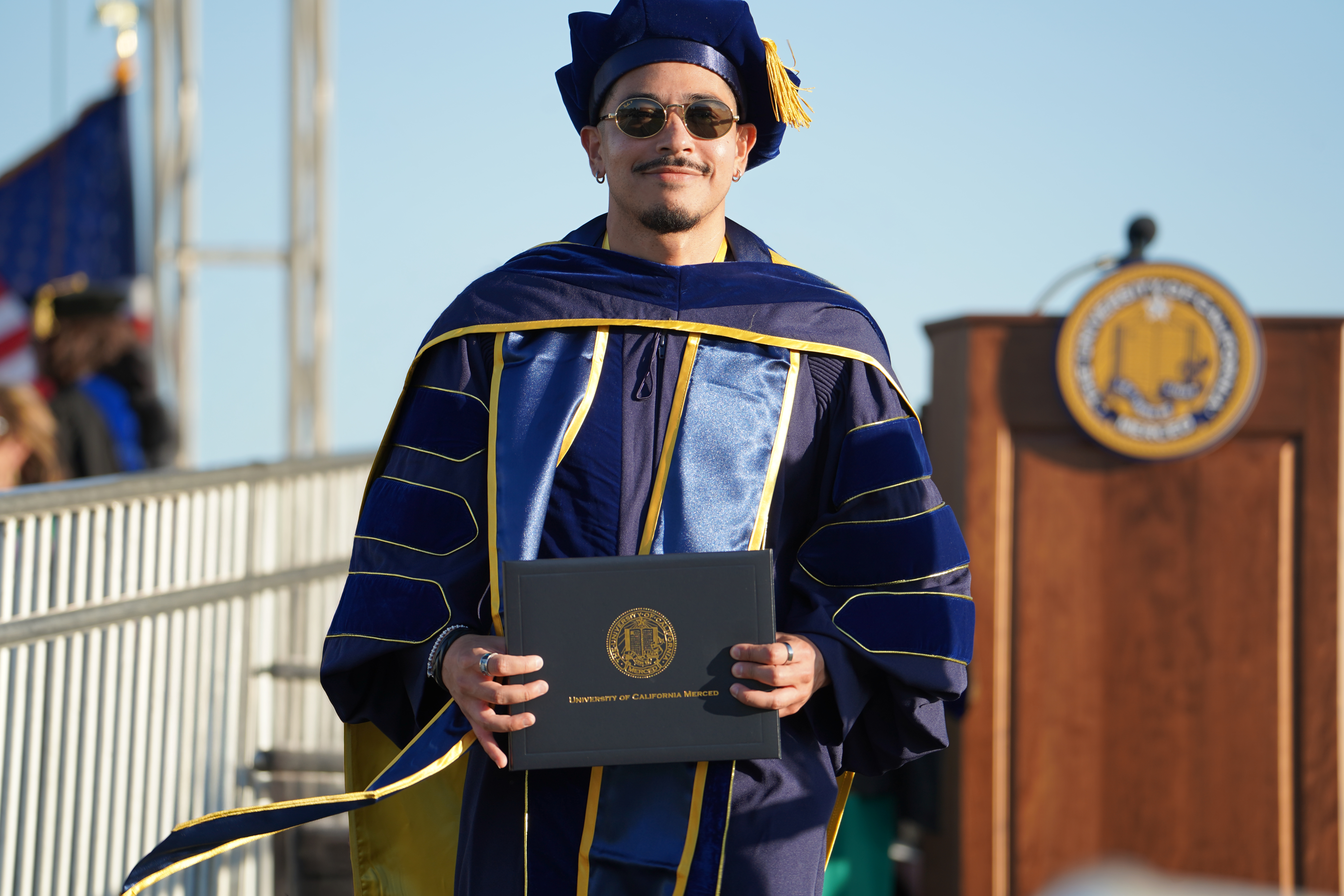 Graduate in cap and gown holding diploma cover at Commencement. 