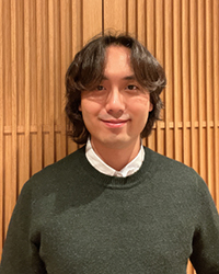 male with brown hair wearing white shirt and green sweater