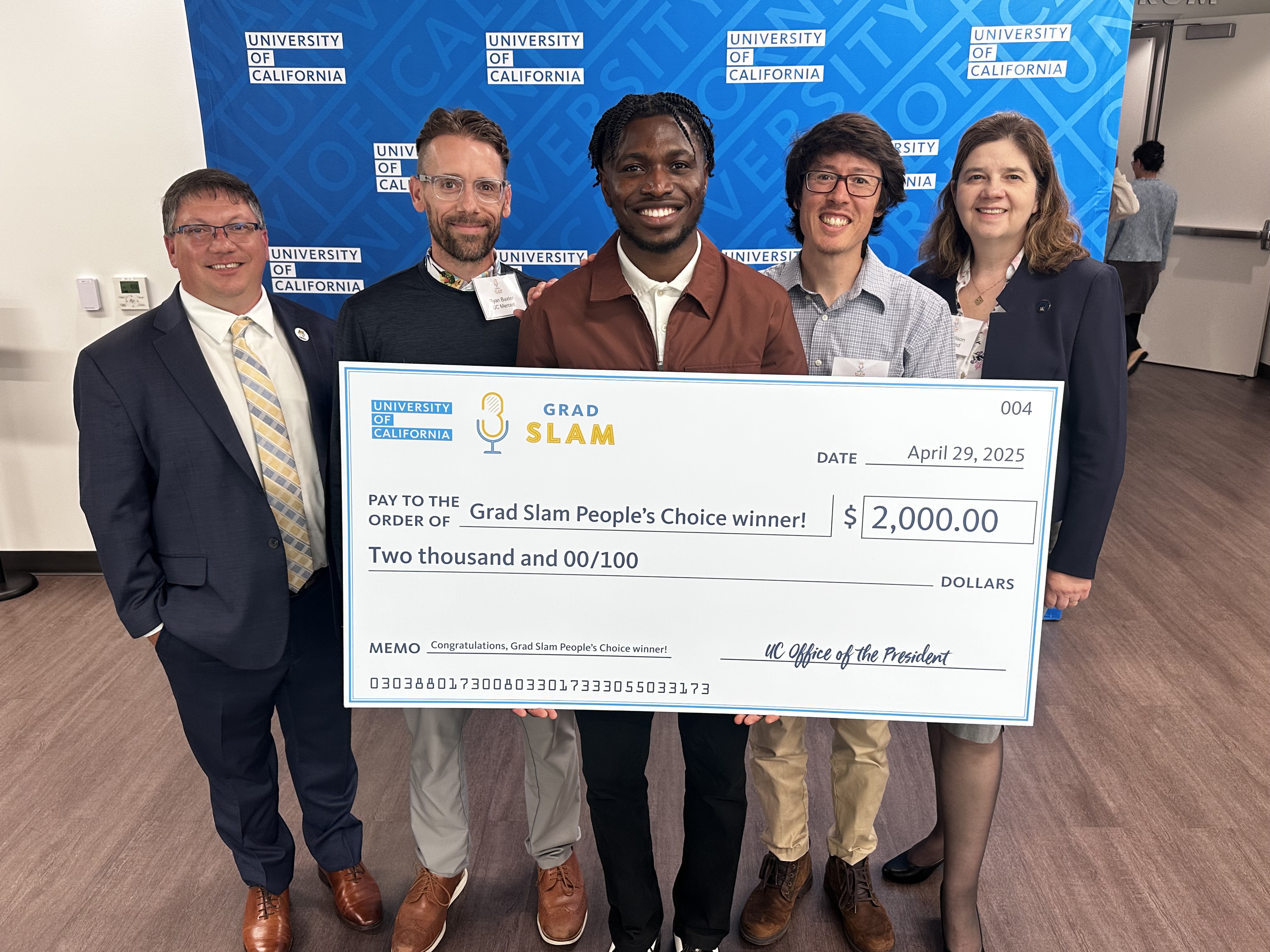 group of five people standing with a large check
