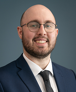male with glasses wearing blue suit and tie