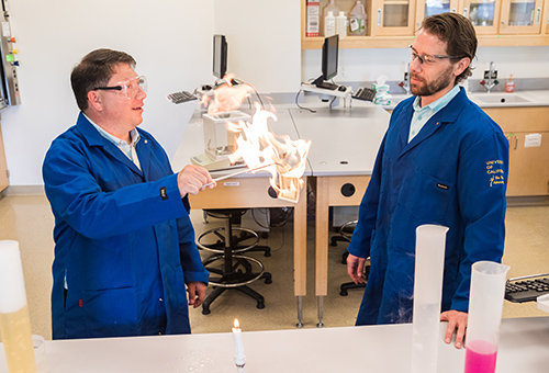 Two professors in a lab with fire on an object.