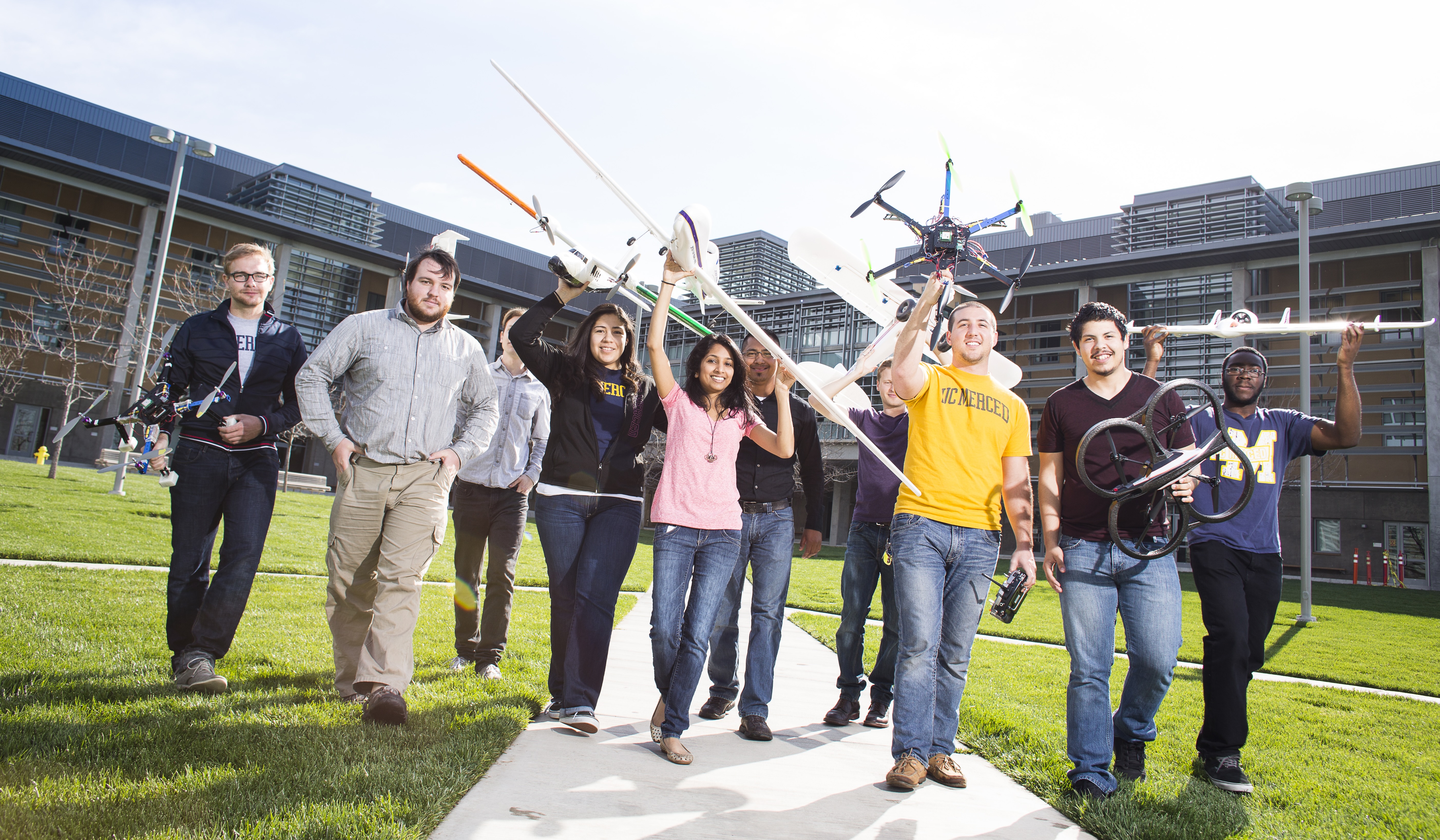 Group of individuals walking across UC Merced's Academic Quad with drones in their hands.