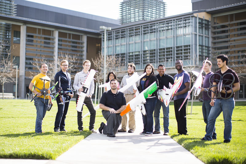 Group of student staning in front of Science and Engineering Building with drones and planes