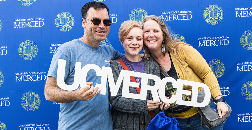 A family takes a photo with a UC Merced sign.