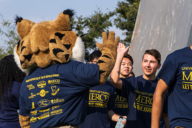 Rear view of a Bobcat mascot high-fiving college students