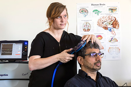 Graduate student Chelsea Gordon, standing, demonstrates transcranial magnetic stimulation on Professor Ramesh Balasubramaniam.